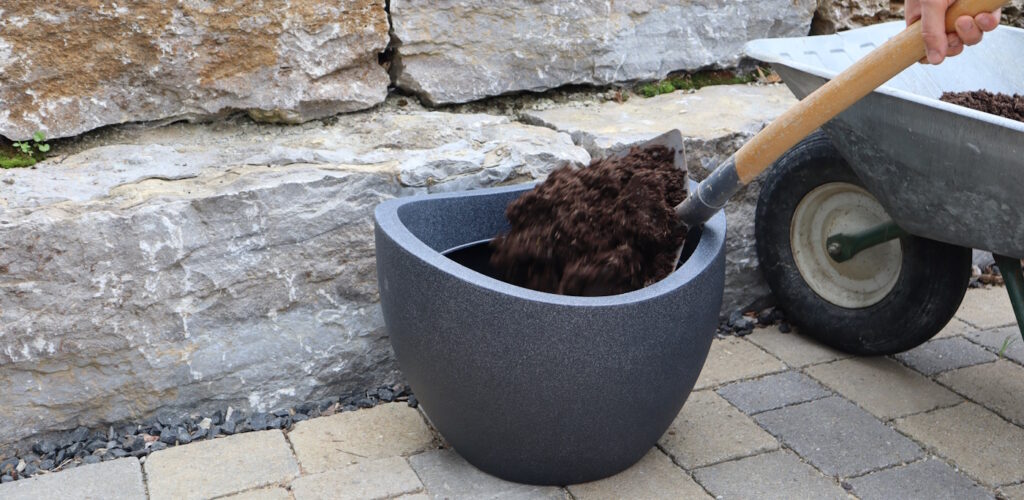 Das Foto zeigt, wie Erde in einen Pflanzkübel geschaufelt wird
