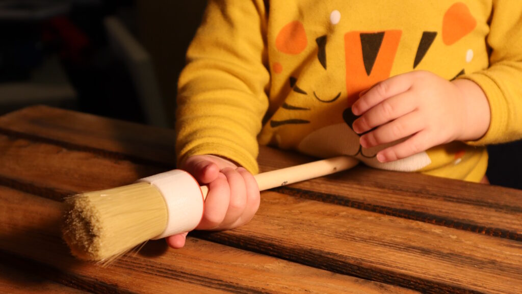 Das Foto zeigt Kinderhände mit einem Pinsel in der Hand