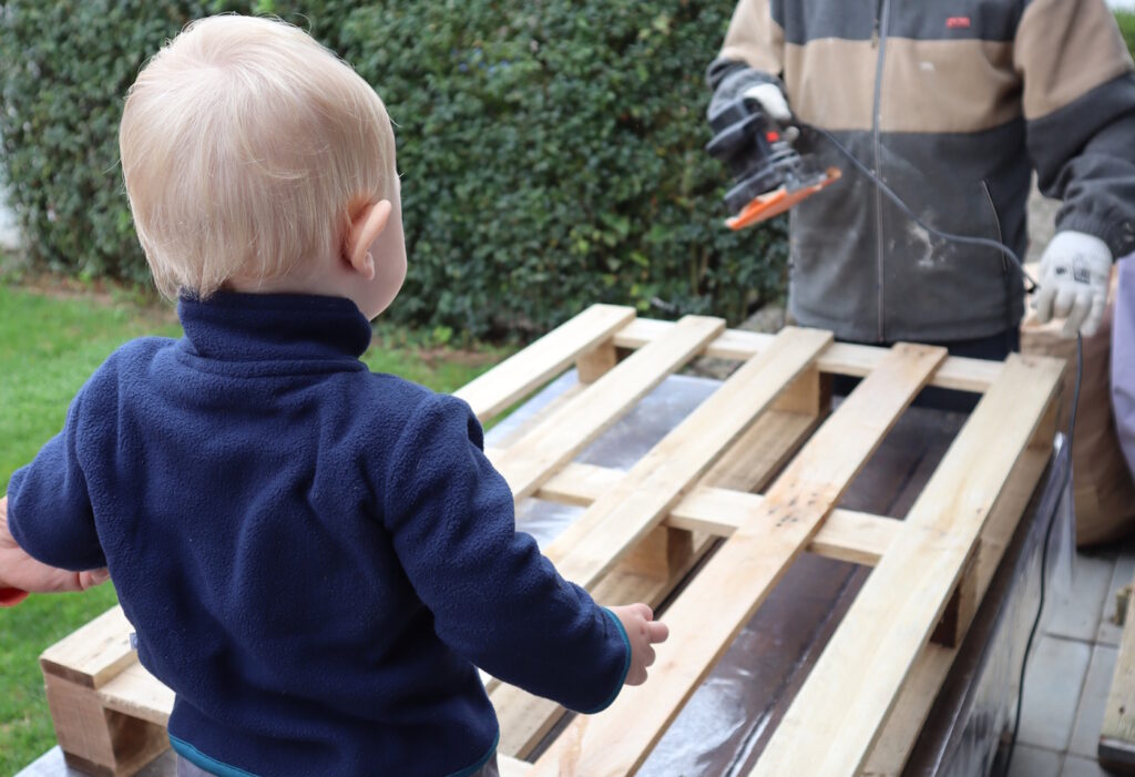 Das Foto zeigt ein Kind, das beim Schleifen einer Palette zuschaut
