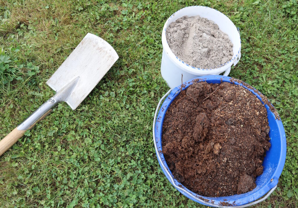 Das Foto zeigt einen Eimer mit Sand und einen Eimer mit Gartenerde