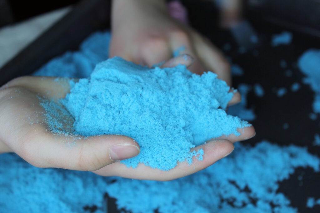 Das Foto zeigt zwei Hände die mit blauem Sand spielen