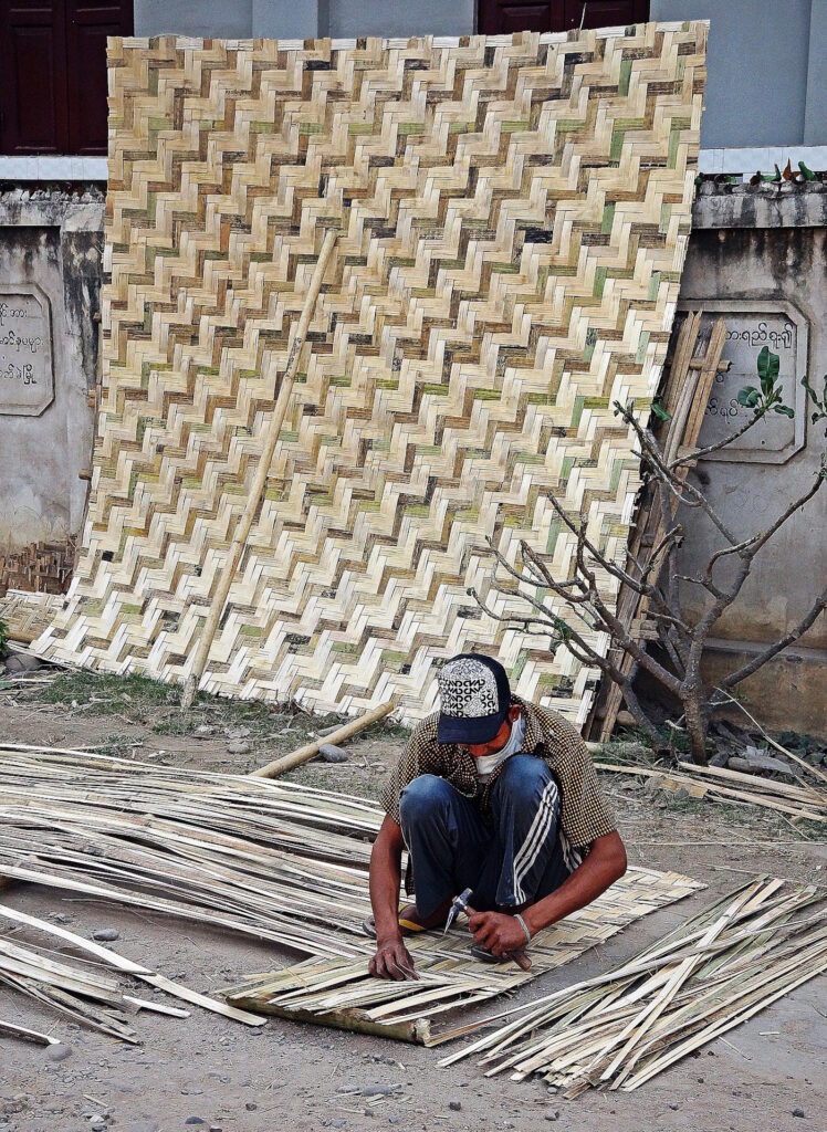 Das Foto zeigt einen Mann der mit Bambus flechtet