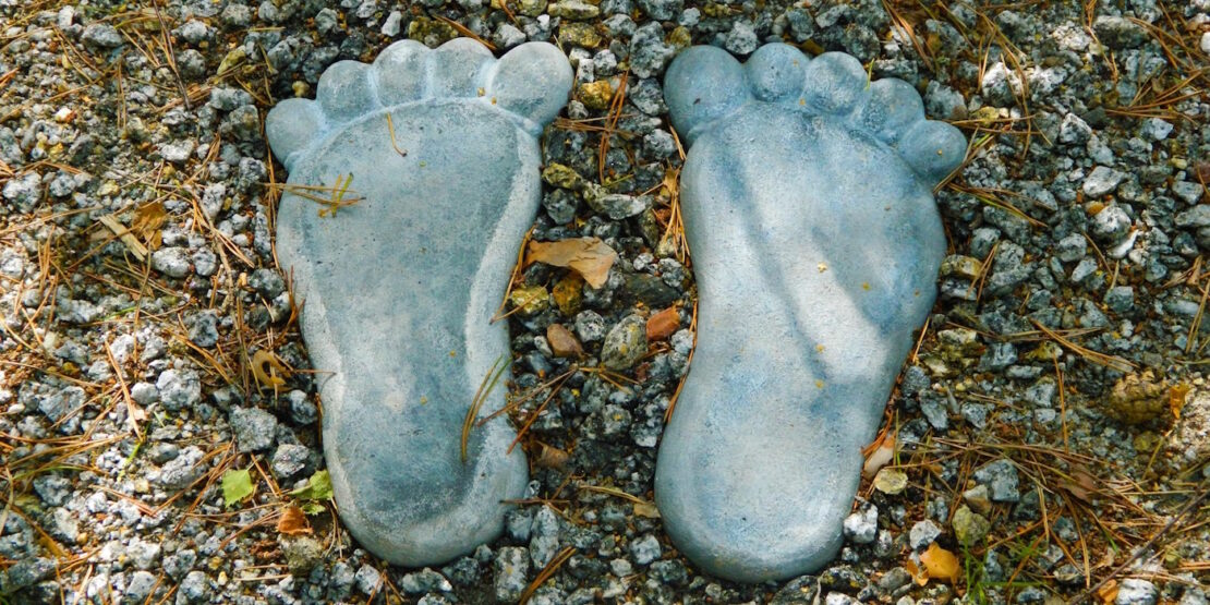Das Foto zeigt zwei Füße aus Stein die in einem Kiesbett liegen