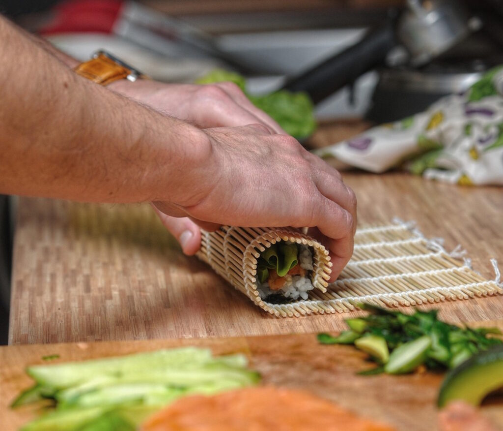 Das Foto zeigt eine Person die mit einer Sushimatte Shushi rollt